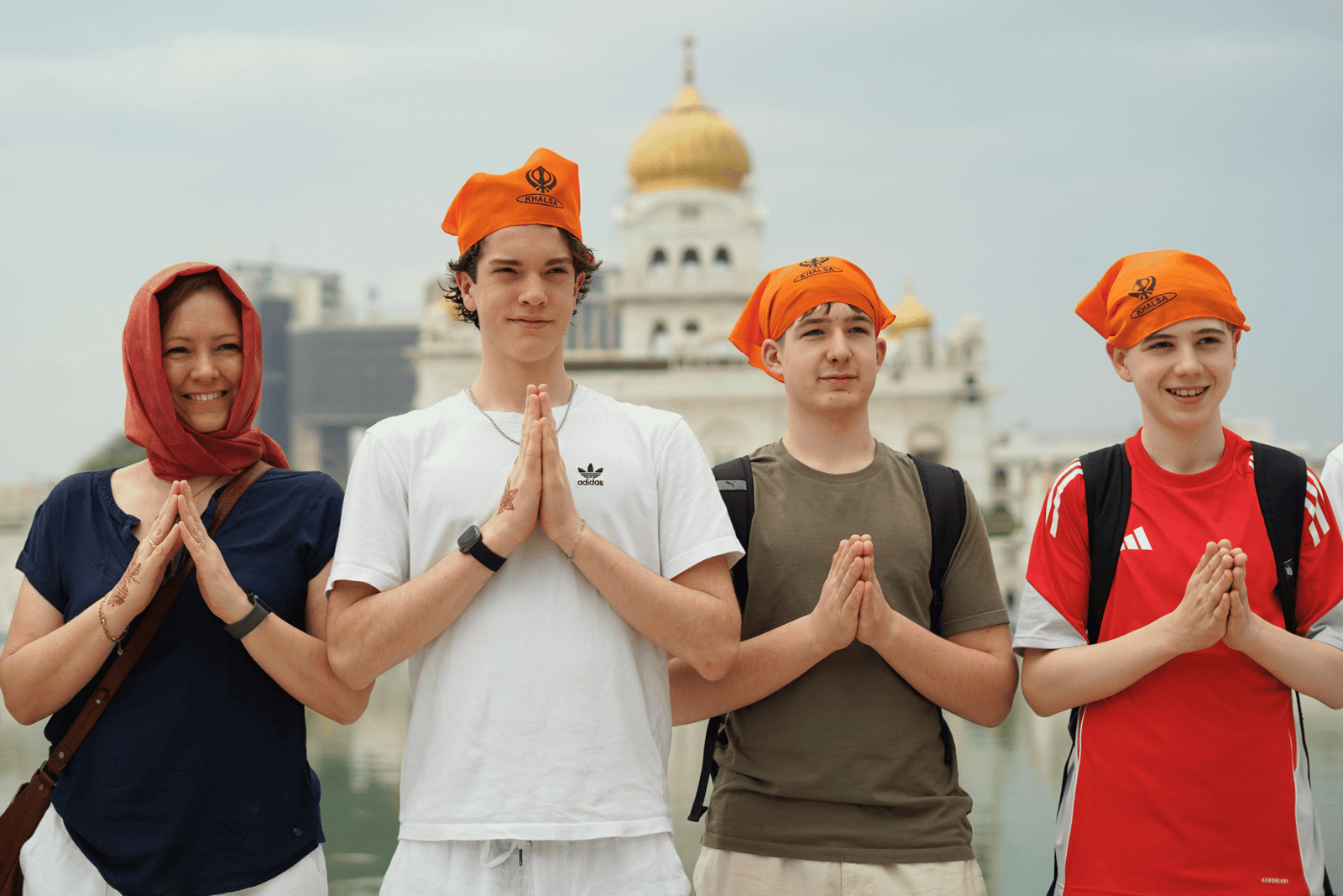 Travelers wearing traditional orange head coverings posing in front of Gurudwara Bangla Sahib, a famous Sikh temple in Delhi.