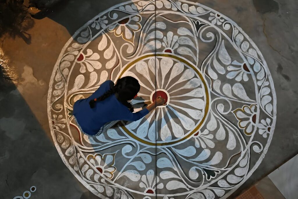 Indian woman creating a traditional white rangoli design on the floor, a ritual believed to protect the home from negative energy and ward off the evil eye.