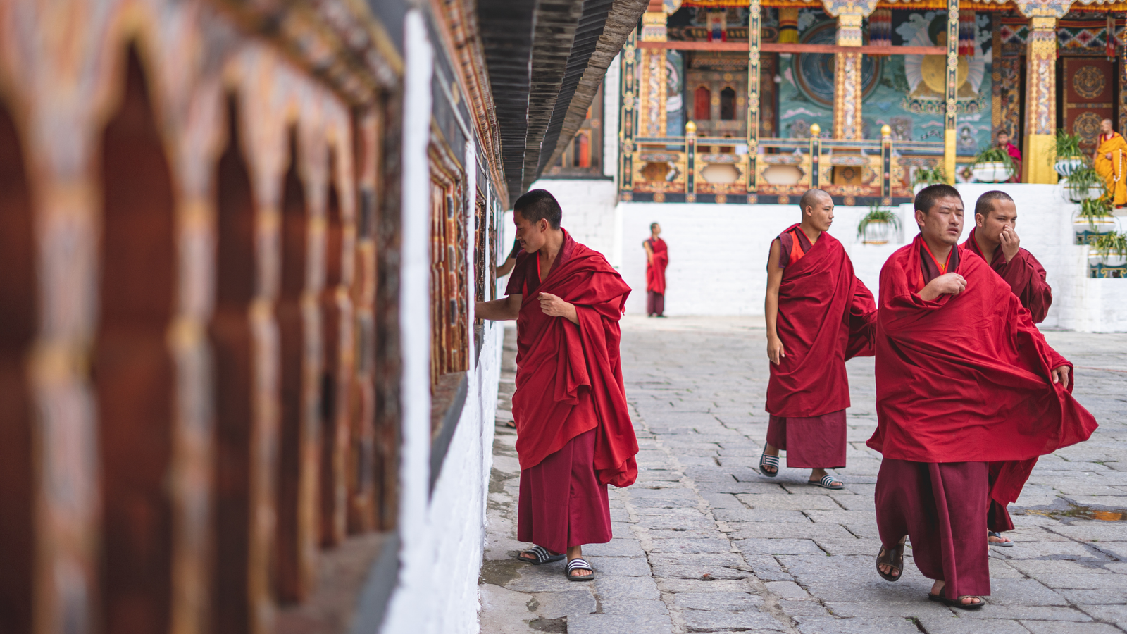 Buddhist monks in red robes walking beside a decorated building in Bhutan