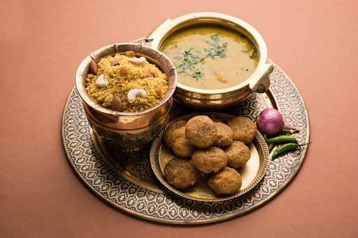 A traditional Rajasthani meal of dal baati churma served in brass bowls, garnished with nuts and herbs on a decorative plate.