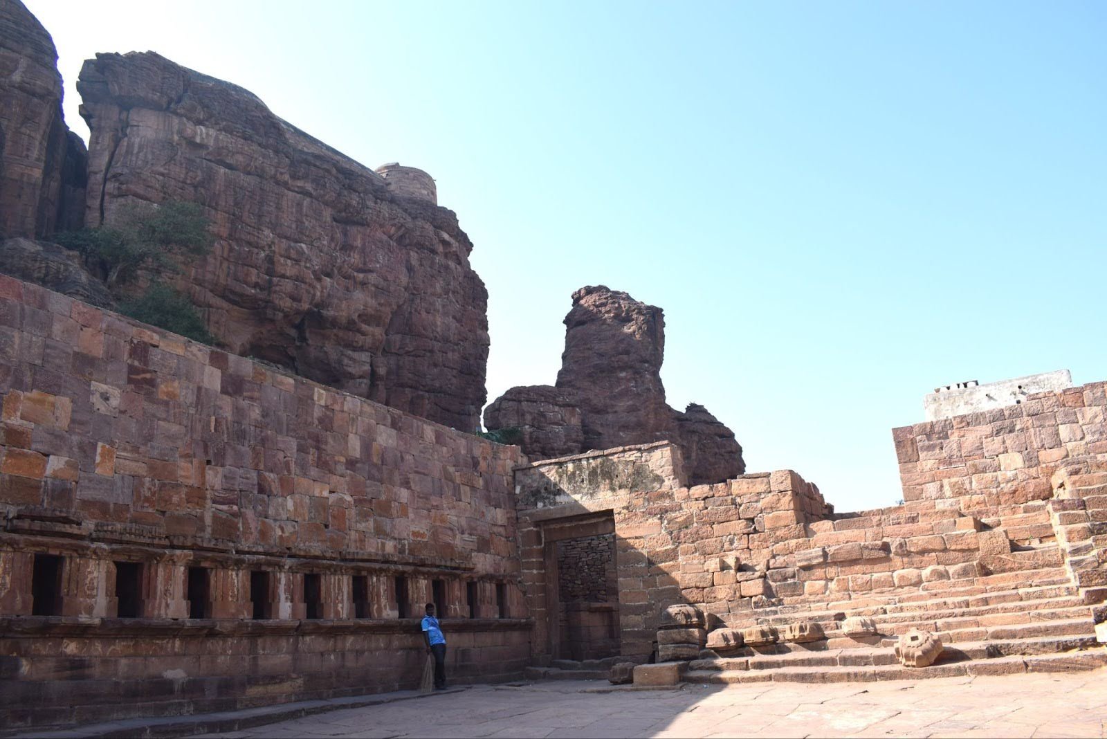 A photo of an ancient stone fortress built into a rugged, reddish-brown cliffside under a pale blue sky.