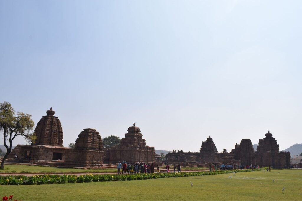 A series of ancient stone temples with intricate spires on a green lawn under a clear sky.