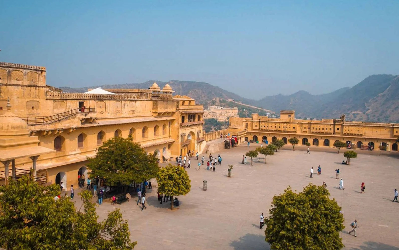 Visitors exploring the courtyard of Amber Fort with the Aravalli hills in the background—travel banner for the Golden Triangle tour itinerary covering Delhi, Agra, and Jaipur in 4 to 7 days.