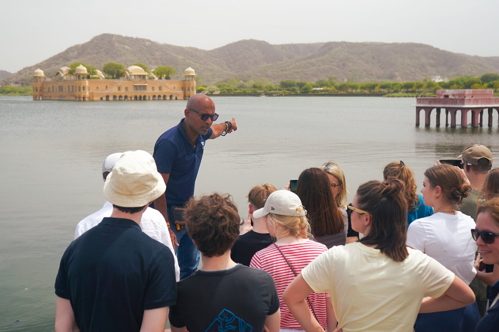 A Reality tour guide points toward the Jal Mahal palace in Jaipur, India, while leading a group of international travelers on a trip to India.