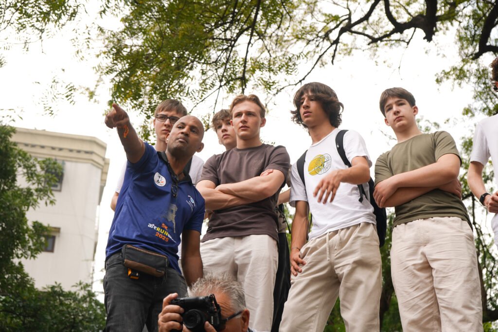 A Reality tour guide in a blue uniform pointing out a landmark to a group of interested tourists during an India city tour.