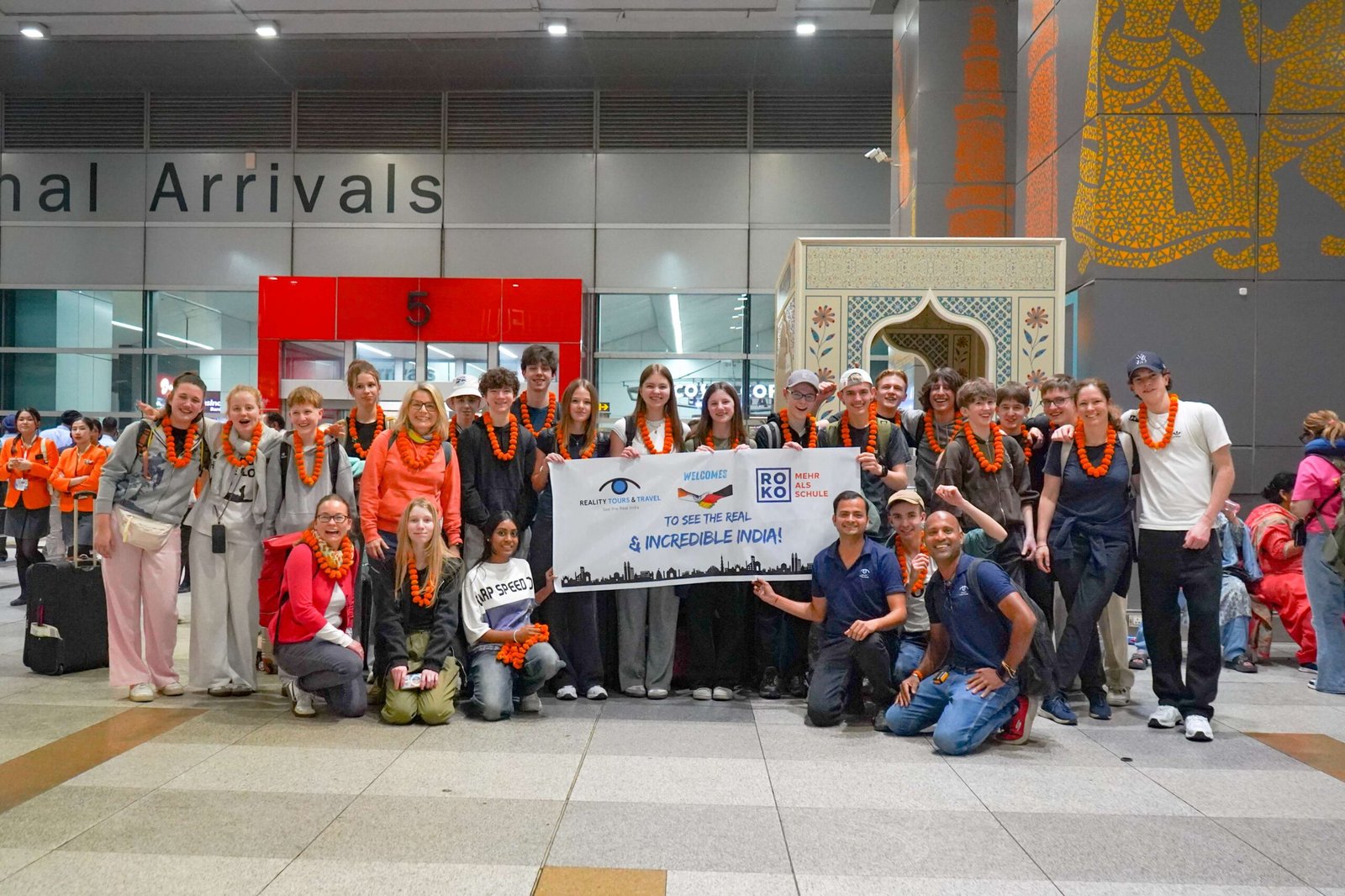 A school and college tour group holding a welcome banner together at an arrival destination in India.