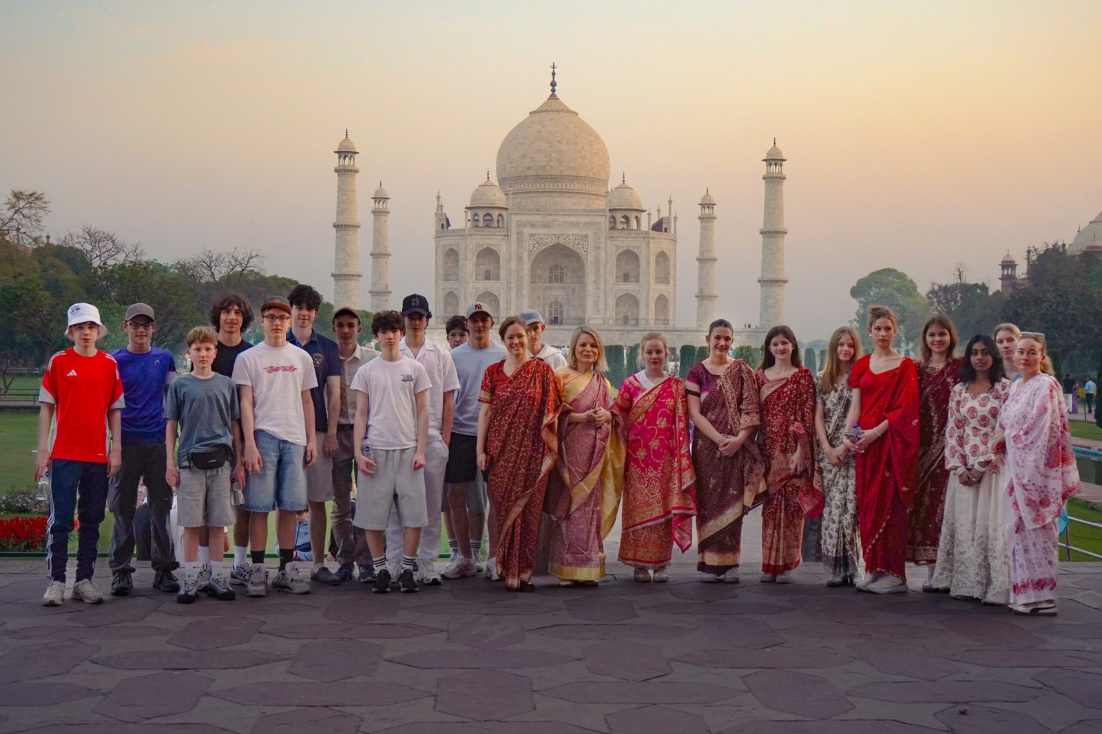 Group of diverse tourists in front of the Taj Mahal at sunset, some wearing traditional Indian attire